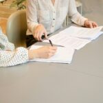 woman signing on white printer paper beside woman about to touch the documents; RMD rules