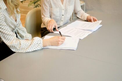 woman signing on white printer paper beside woman about to touch the documents; RMD rules