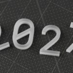White three-dimensional numbers 2027 on a dark grey grid cutting mat; 2027 Social Security earnings limit