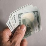 A hand holding a fan of us hundred dollar bills; $6,000 senior deduction