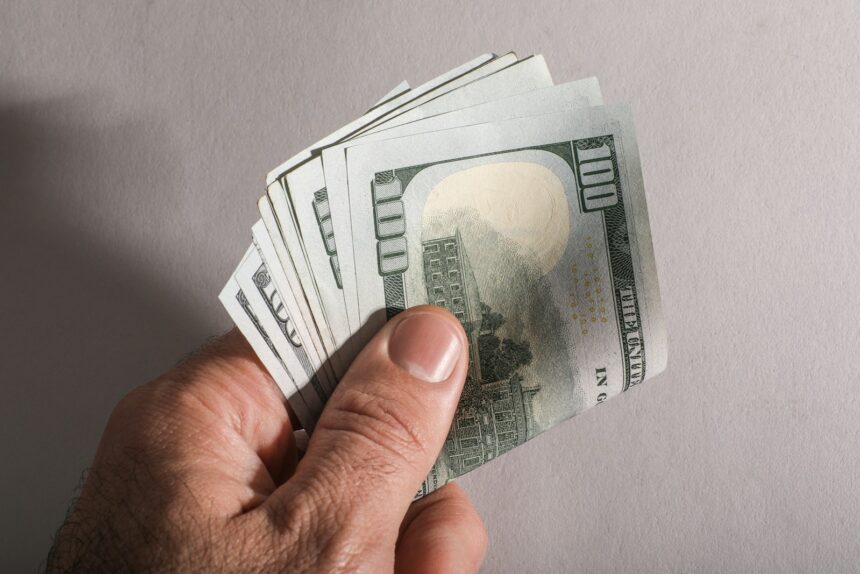 A hand holding a fan of us hundred dollar bills; $6,000 senior deduction